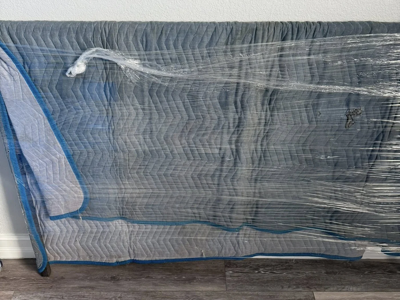 Large household item wrapped with a moving blanket and protective film
